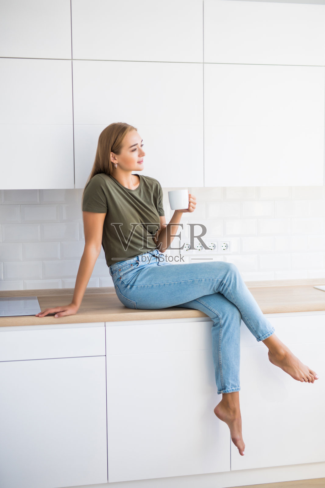 年轻漂亮的女人拿着咖啡或茶，坐在厨房的柜台上照片摄影图片