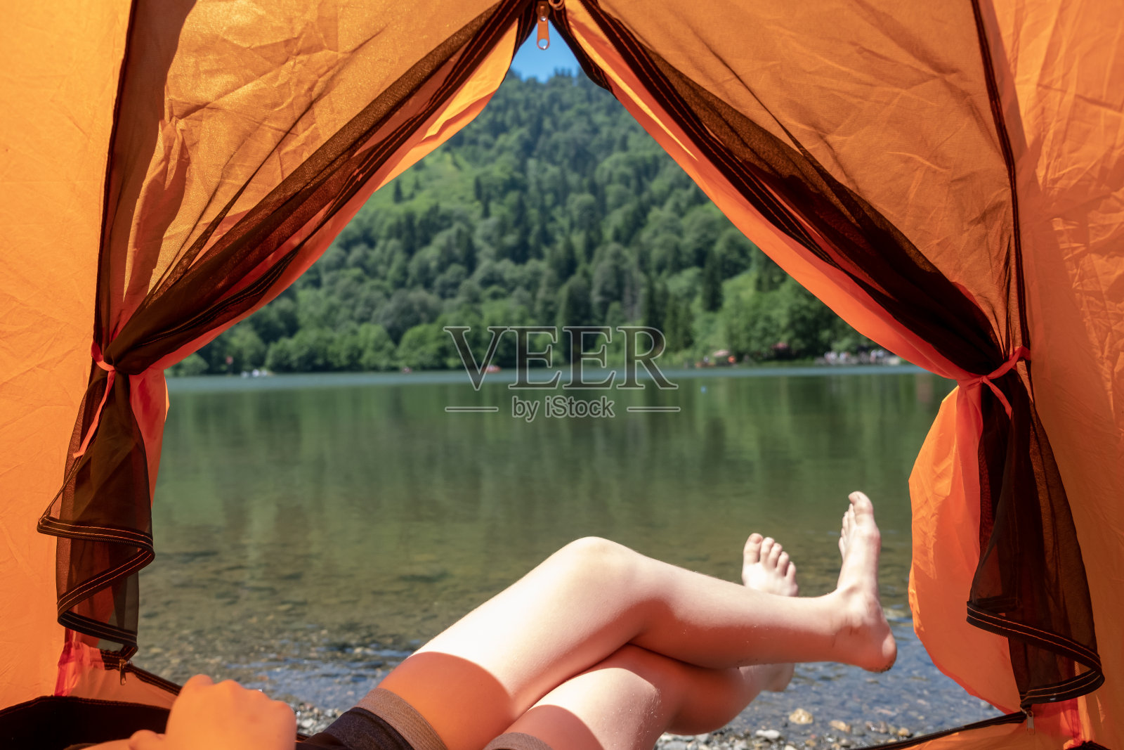 一个女孩坐在帐篷里，后面是一个令人难以置信的湖照片摄影图片