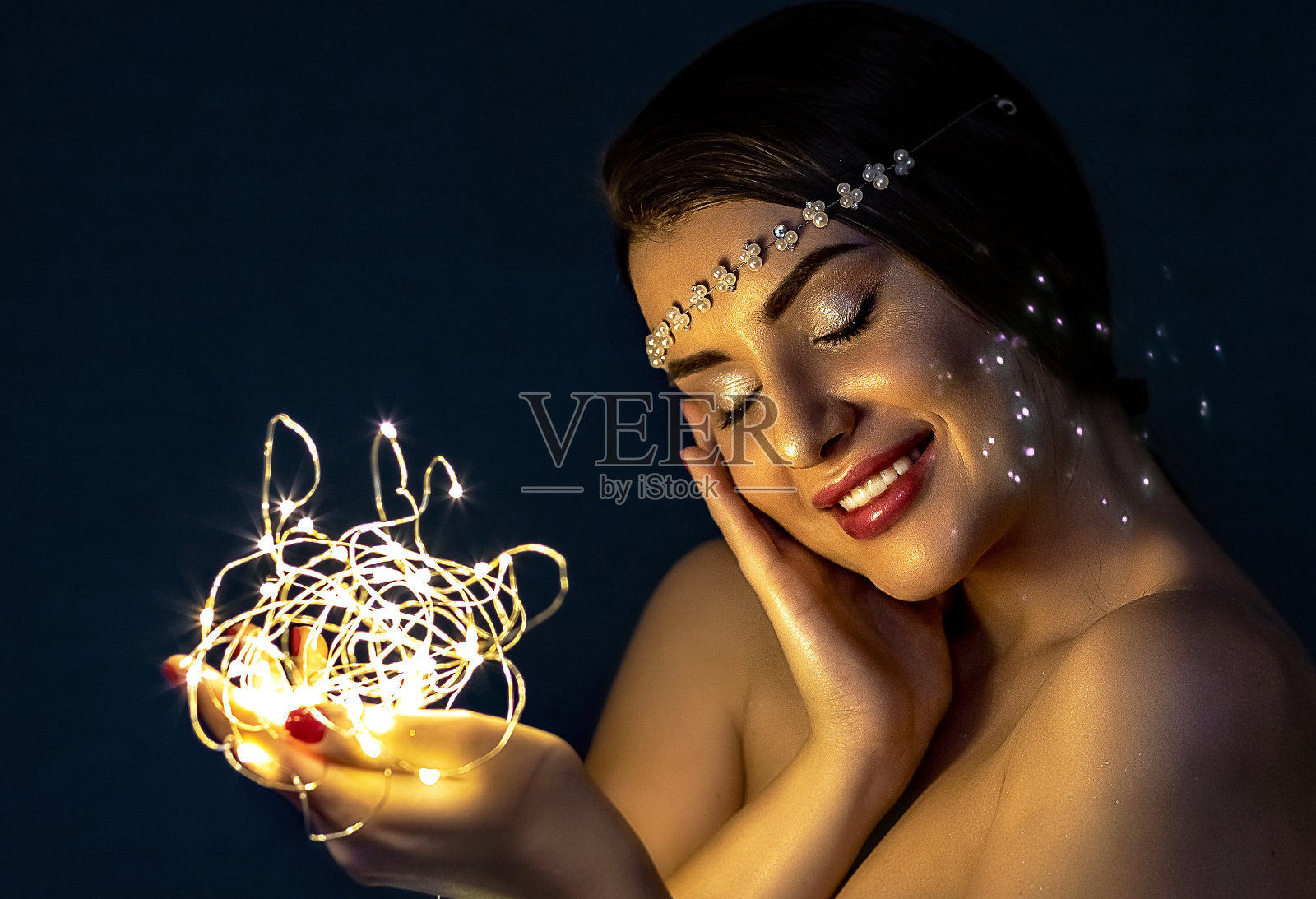 一个黑发的女孩，在蓝色背景的夜晚，手里拿着火花，甜蜜地微笑着。照片摄影图片