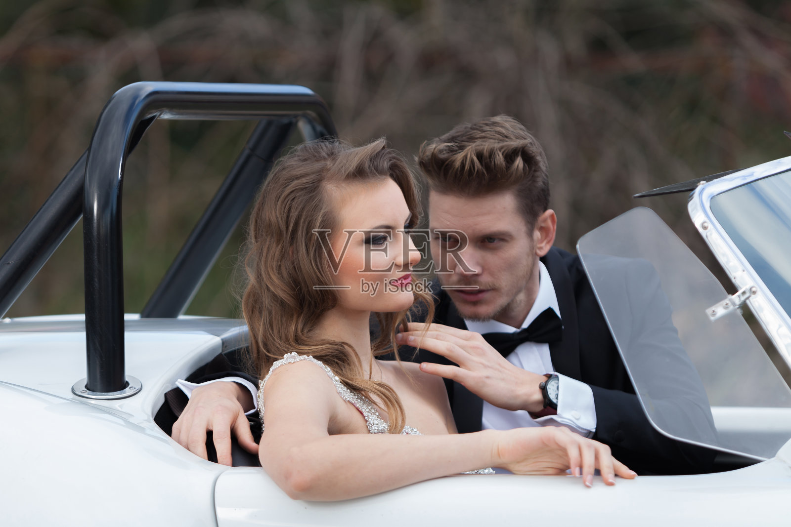 一对优雅的年轻夫妇坐在白色老爷车旁照片摄影图片