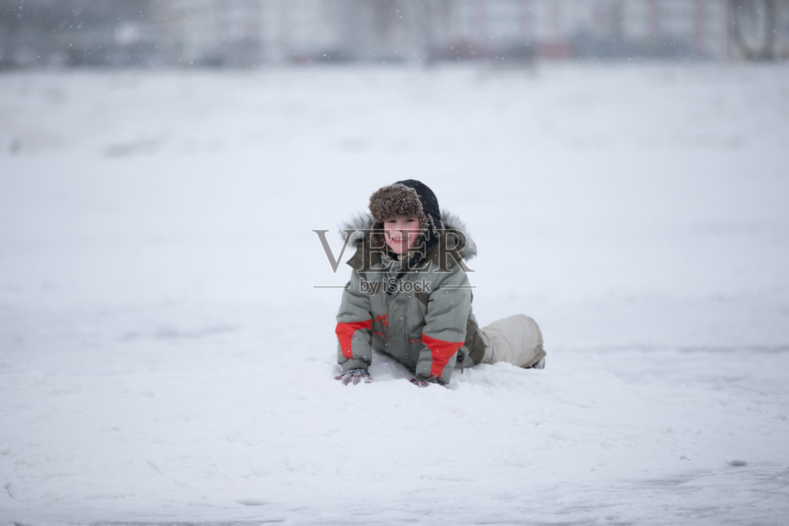 一个孩子在雪中快乐地玩耍。冬天里戴着皮帽的男孩照片摄影图片
