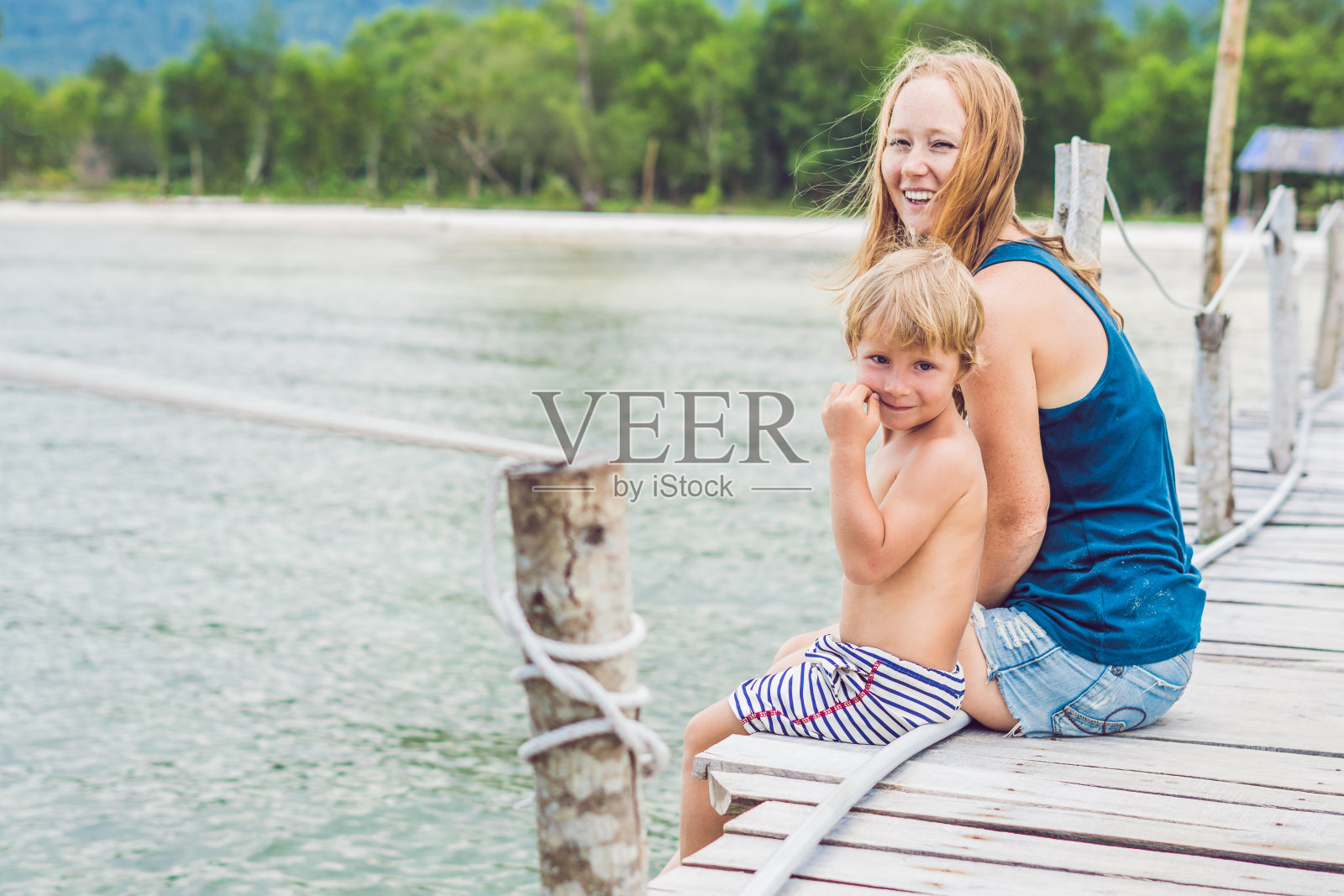 妈妈和儿子坐在老码头上，享受着大海照片摄影图片