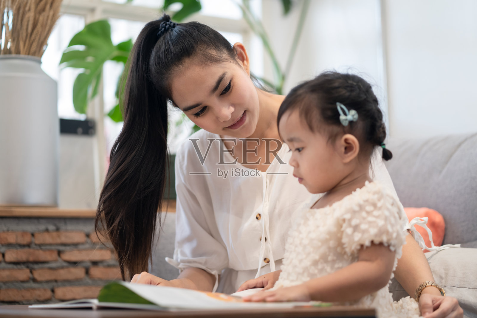 亚洲漂亮的年轻母亲和她的女儿一起读故事书。妈妈高兴地看着小女孩。良好的母子关系。家庭活动与教育理念。照片摄影图片