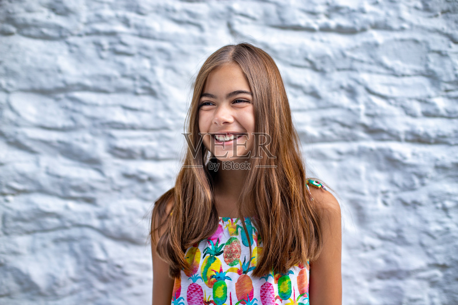 一个在白色石墙前笑着的可爱女孩的肖像。照片摄影图片
