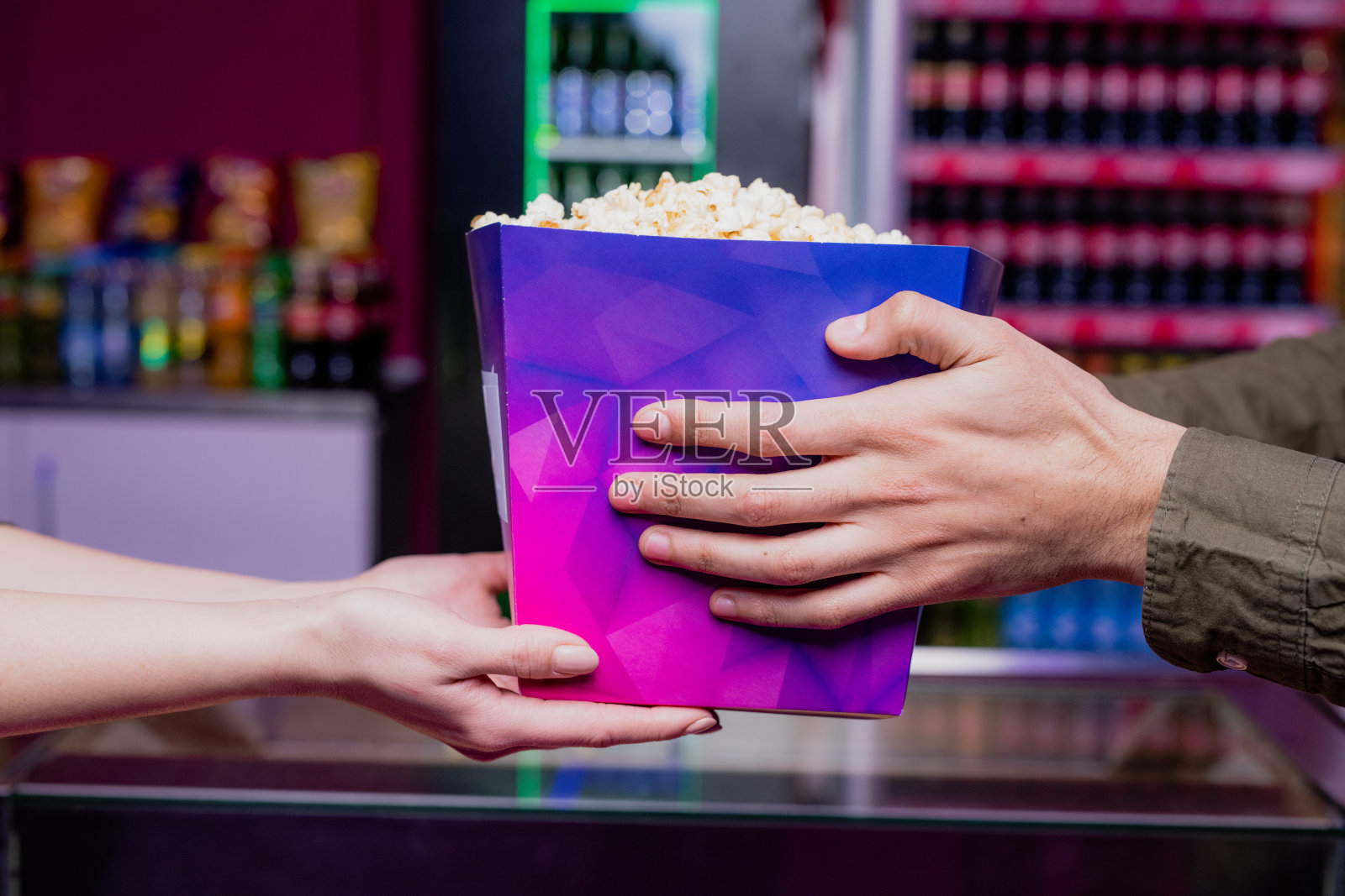 一个年轻人的手拿着一个装满爆米花的紫色大纸盒在电影院照片摄影图片