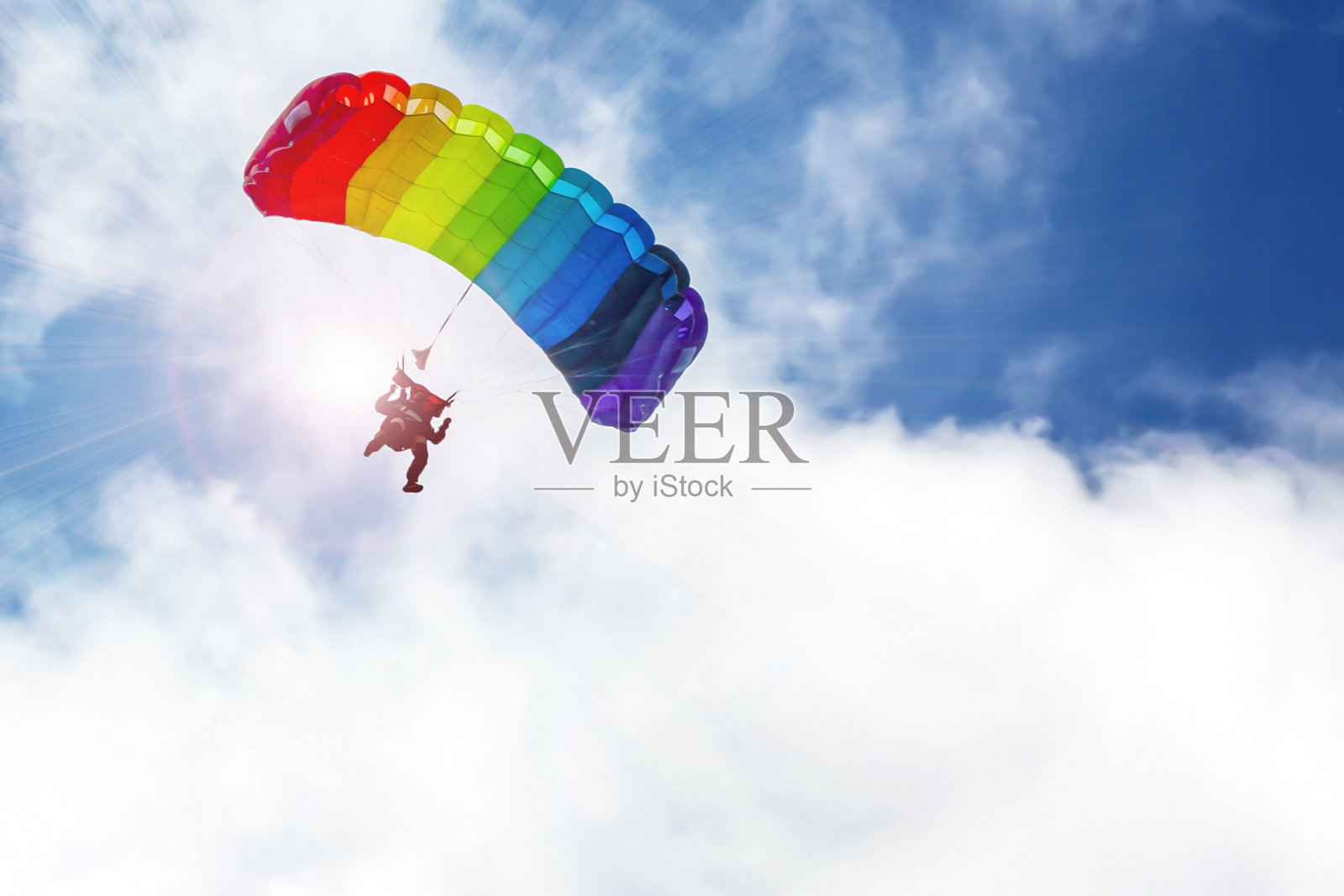 跳伞者在阳光下，乘着降落伞，在天空中飞行，呈现出彩虹般的色彩。照片摄影图片