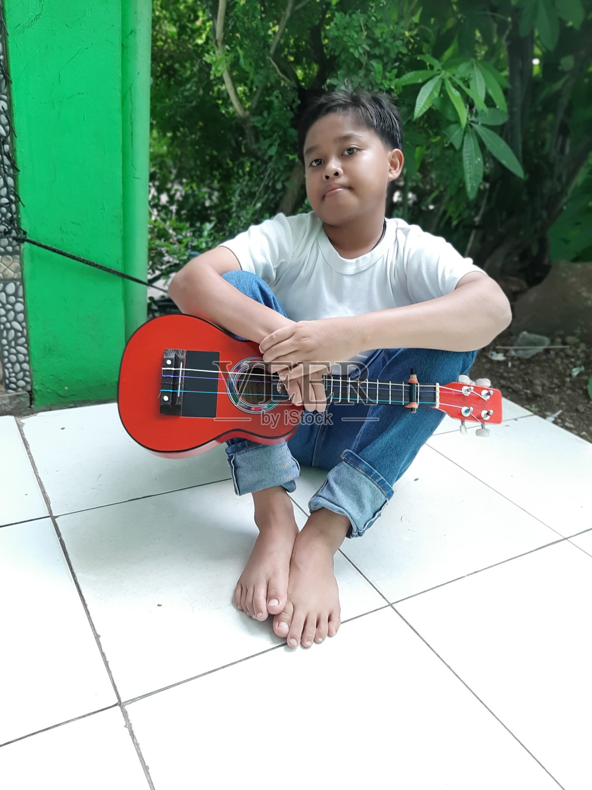 一个年轻的印尼男孩正在弹他的曼陀林吉他。这是一个宁静的阳光明媚的日子，他享受着他在户外的安静时光，他演奏着音乐。照片摄影图片
