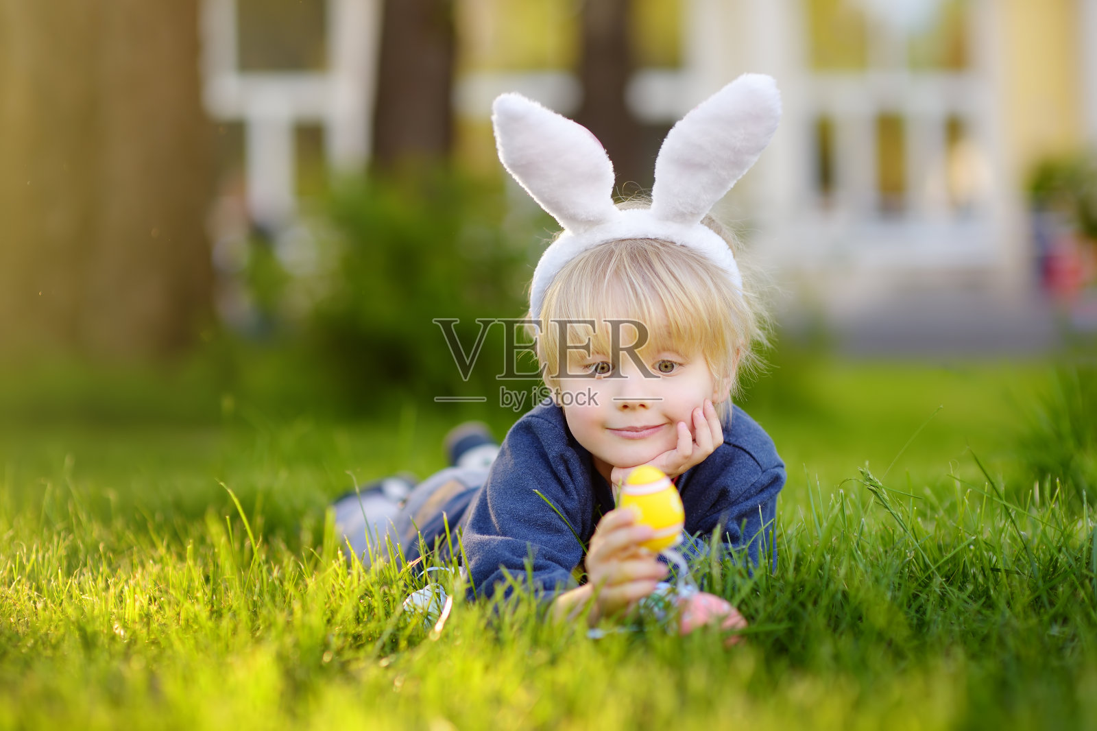 可爱的小男孩戴着兔子耳朵在春天公园里寻找复活节彩蛋。照片摄影图片