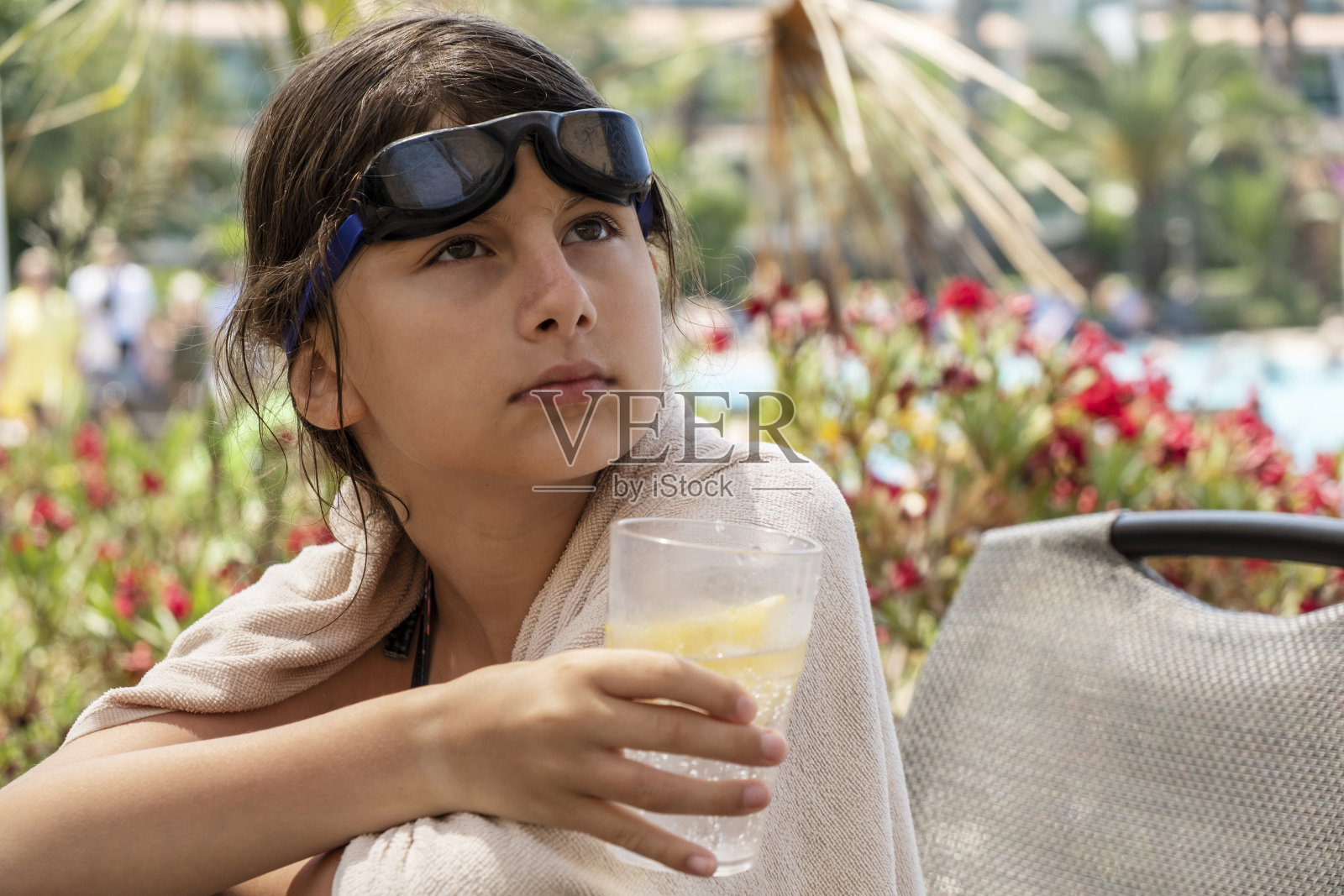 一个10岁的小女孩在泳池边喝着柠檬汽水，想着。照片摄影图片