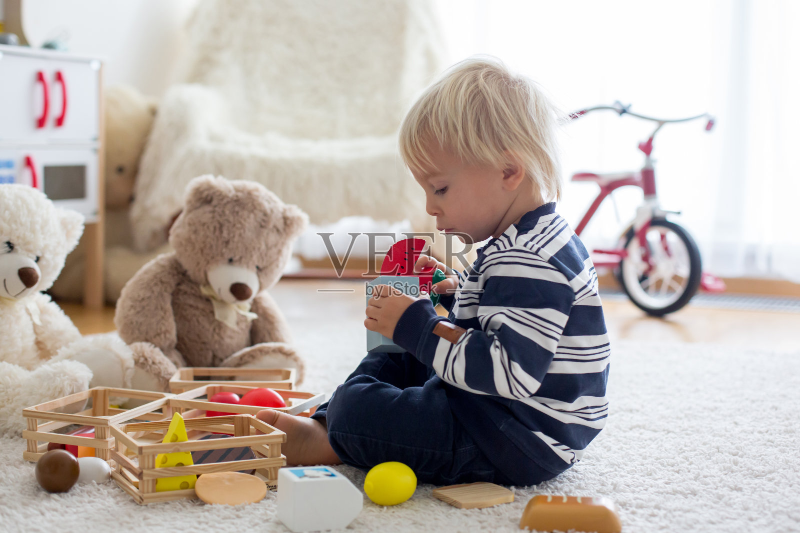 可爱的蹒跚学步的男孩，玩玩具熊和木制玩具从儿童厨房照片摄影图片