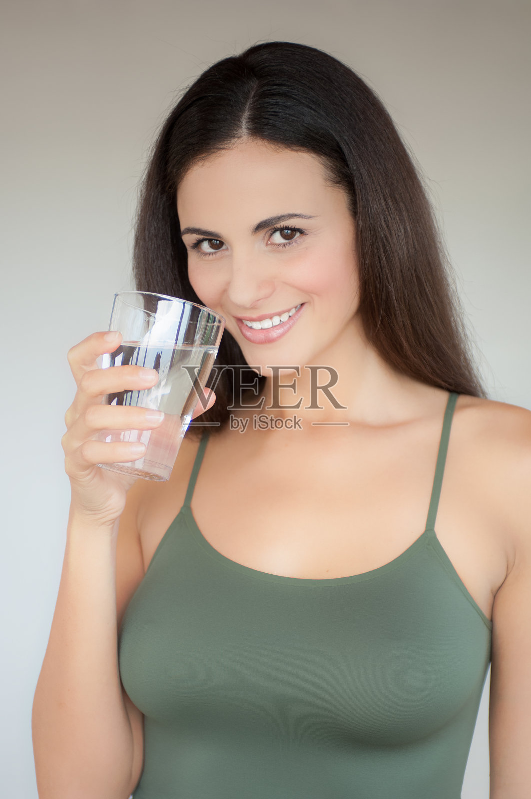 年轻女子穿着绿色衬衫，微笑着喝着一杯水照片摄影图片