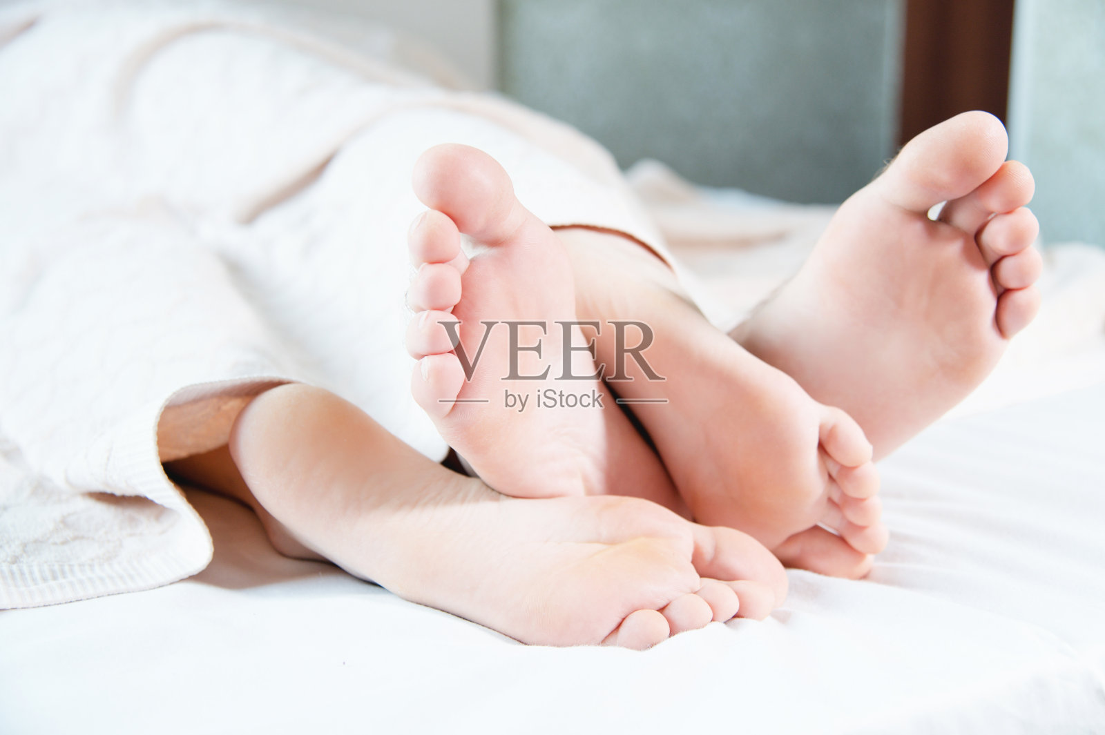 一对年轻夫妇的脚的特写，从卧室的被窝里伸出来。光着的脚互相抚摸，在梳妆打扮。照片摄影图片