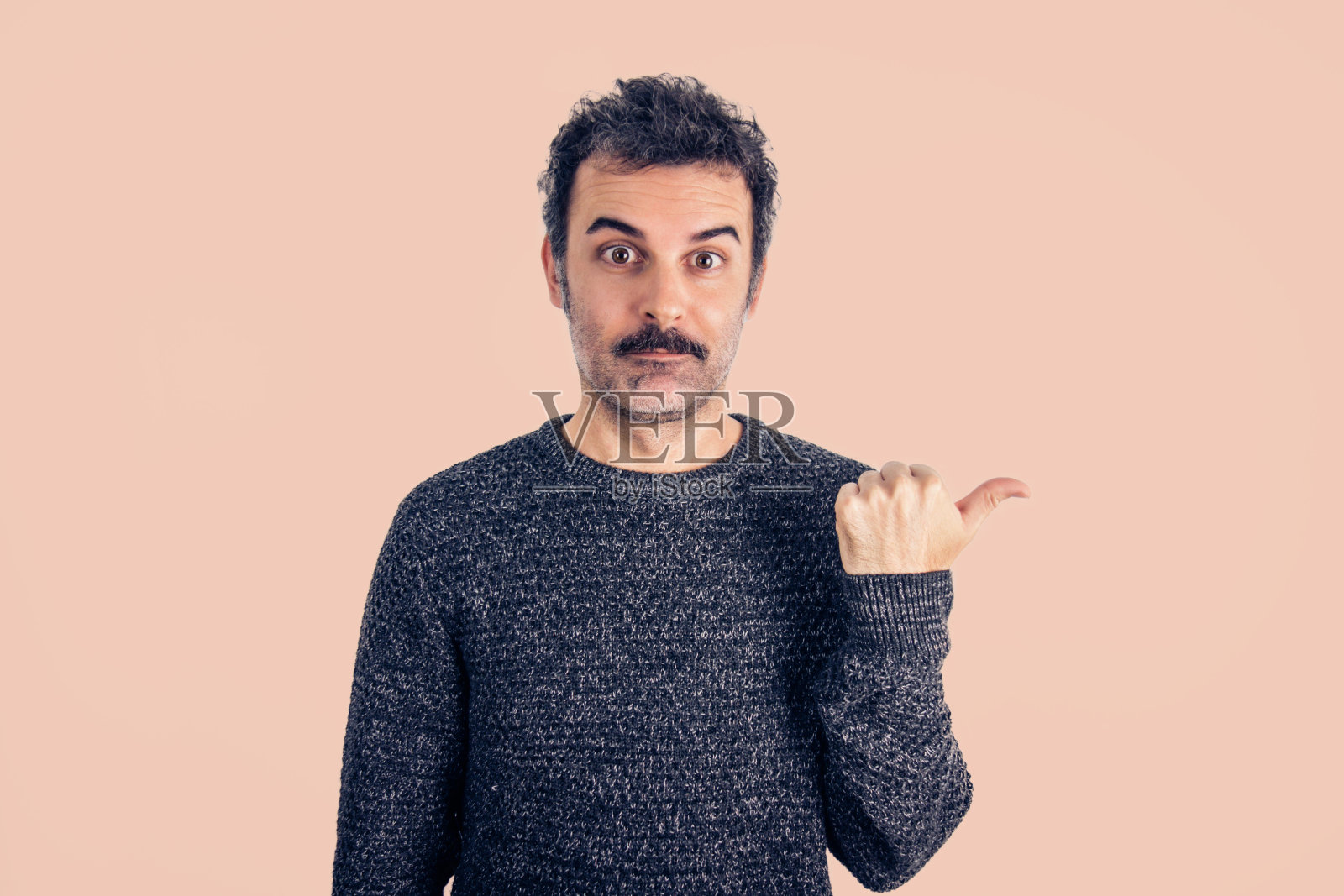 一个棕色的，留着胡子和灰色毛衣的英俊男子的肖像用拇指指着。照片摄影图片