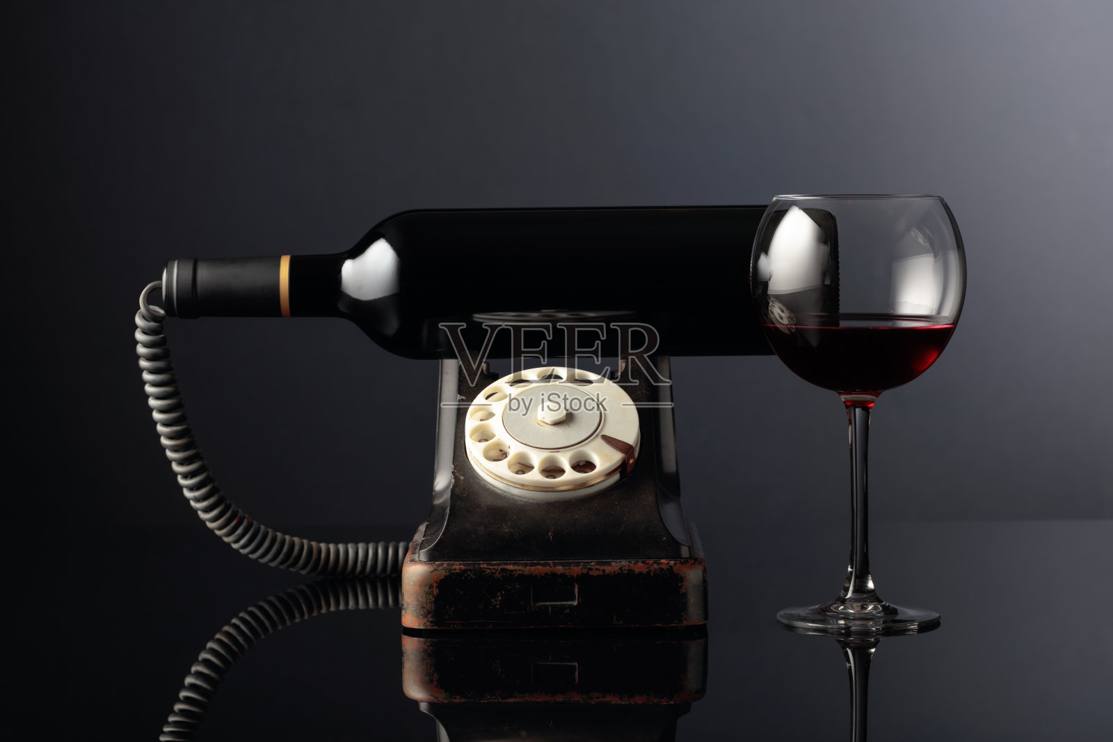 旧的黑色手机和红酒在黑色的反光背景上。概念的形象。照片摄影图片