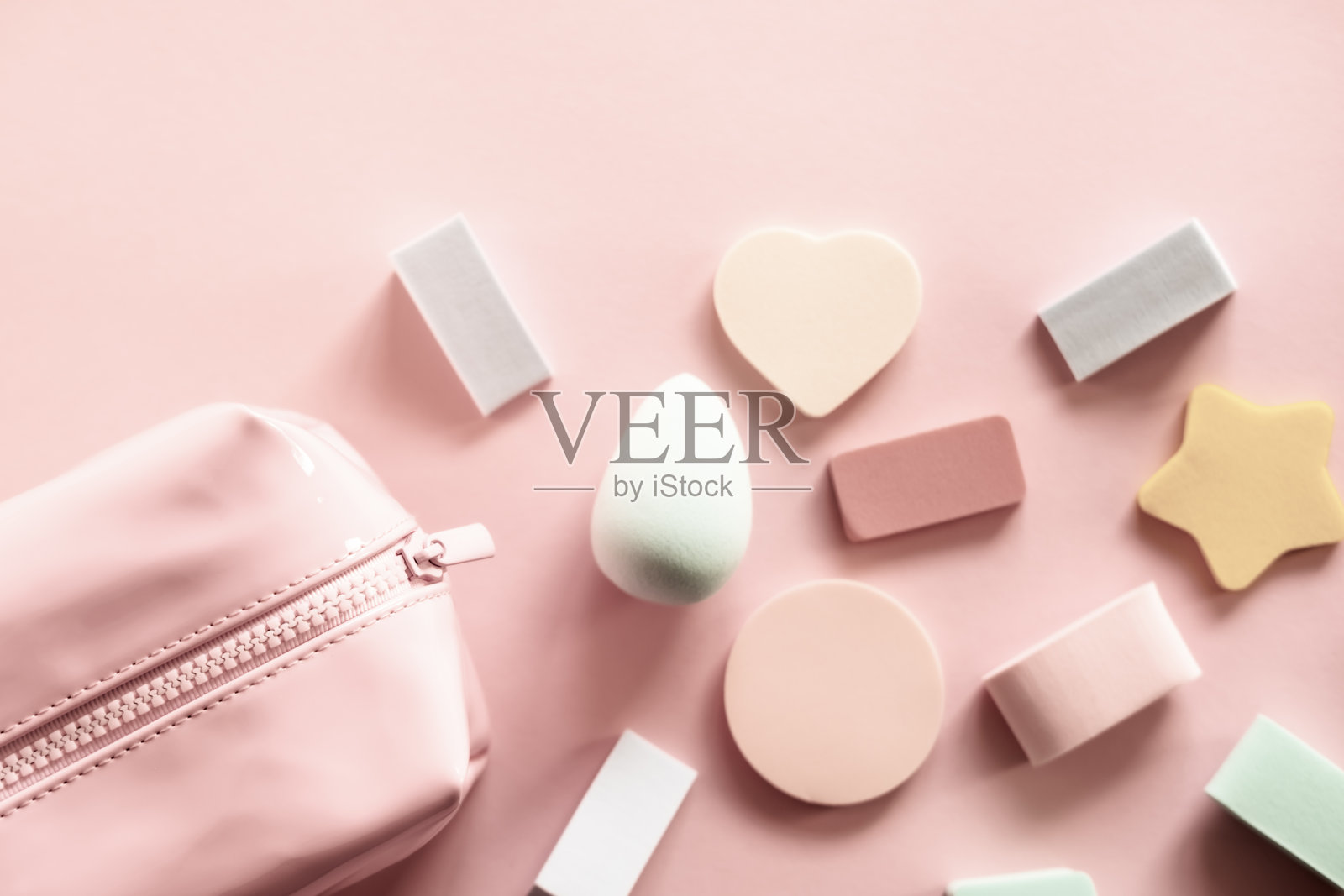 粉彩背景上的粉色化妆包、美容产品和不同形状的海绵。皮肤护理的概念。照片摄影图片