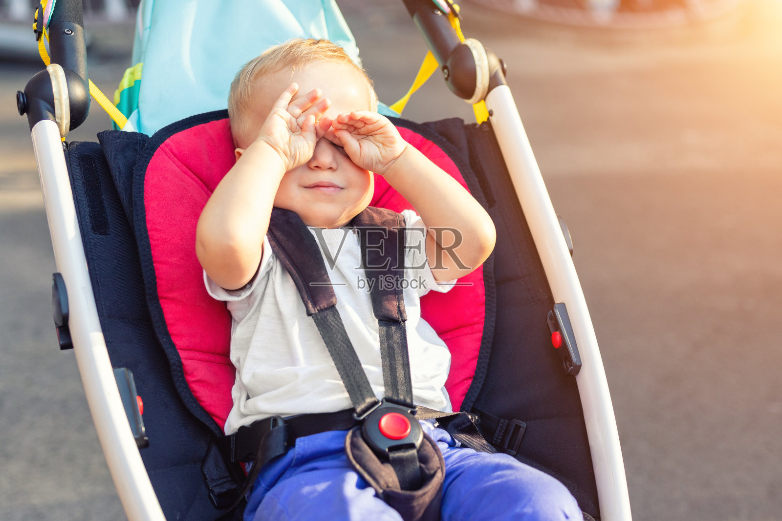 在阳光明媚的夏日户外，可爱可爱的蹒跚学步的小男孩坐在婴儿车里揉眼睛。累了的孩子想在马车外面走路时睡觉。宝宝想要打盹照片摄影图片
