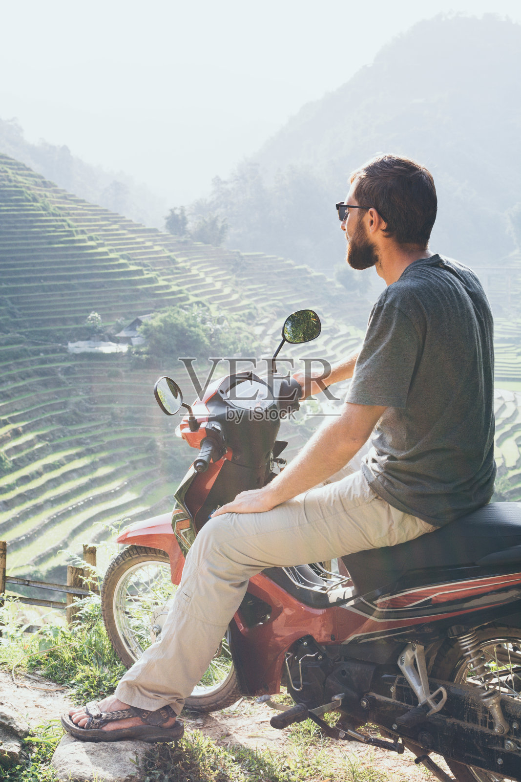 越南老街地区，一名长着胡子的年轻人骑着红色摩托车俯瞰萨帕的稻田照片摄影图片