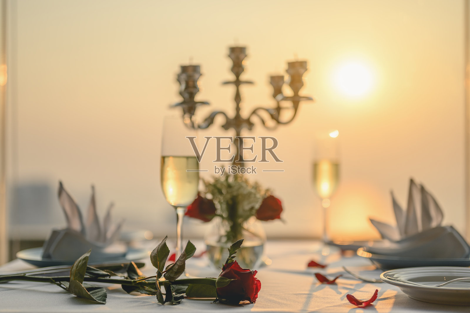 情人节晚餐桌上的玫瑰配上酒杯和烛台。高楼大厦的日落景色。情人节，情侣，蜜月，晚餐，葡萄酒，浪漫的概念。照片摄影图片