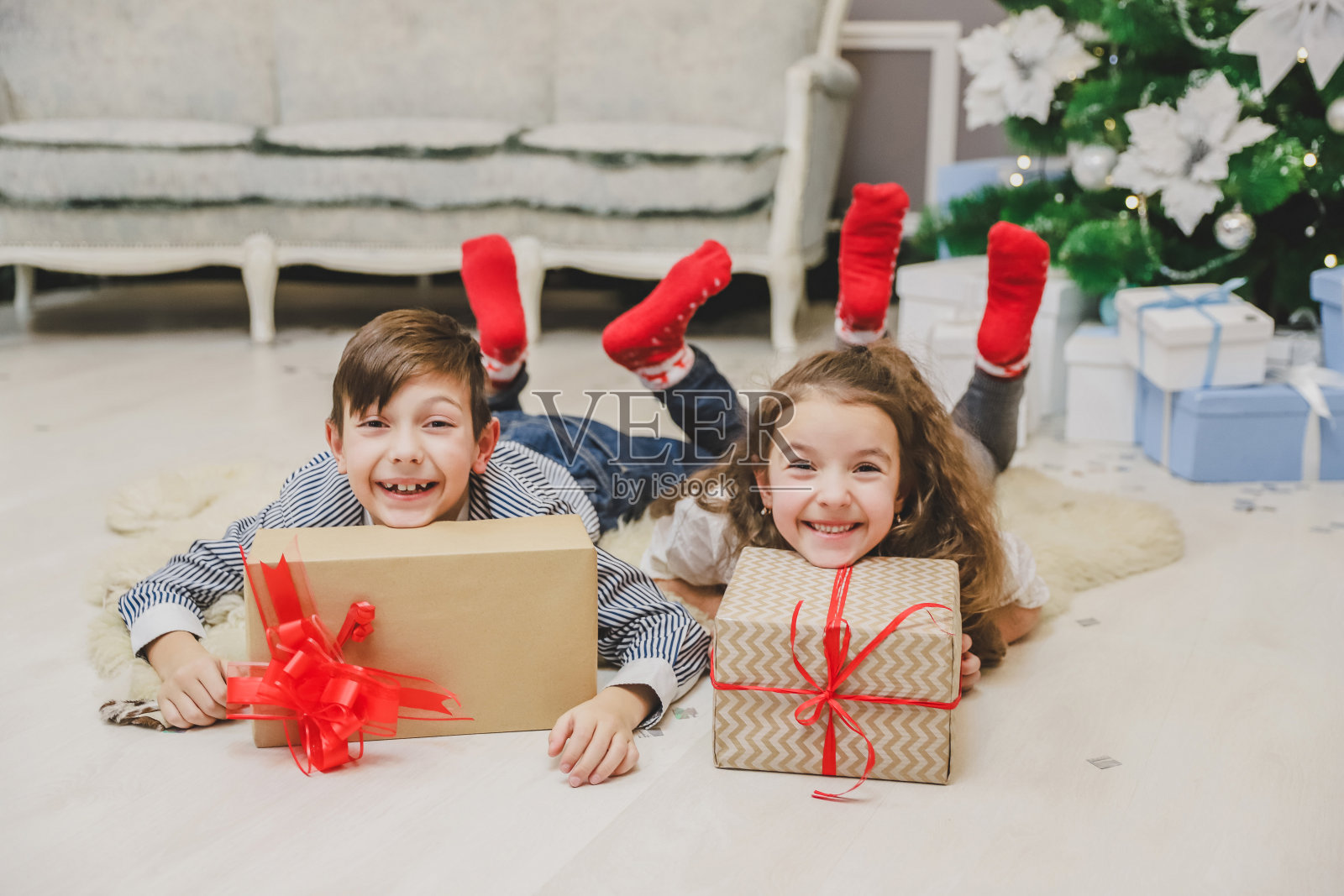 无忧无虑，微笑的小兄弟姐妹享受圣诞时光和礼物，躺在杉树下的地毯上。照片摄影图片
