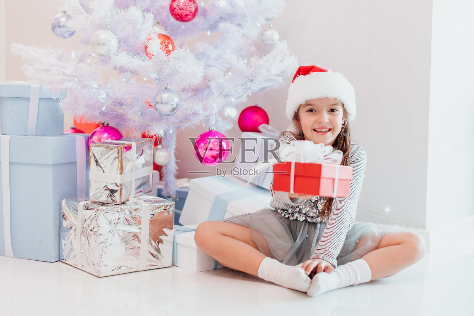 微笑的圣诞老人坐在冷杉树下，把包裹好的圣诞礼物递给镜头。照片摄影图片
