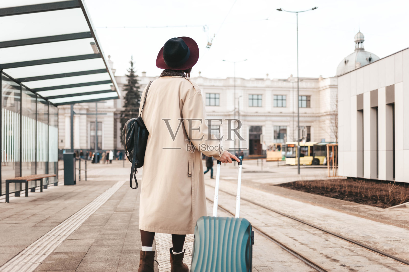时髦的女孩提着行李箱站在城市车站等电车照片摄影图片