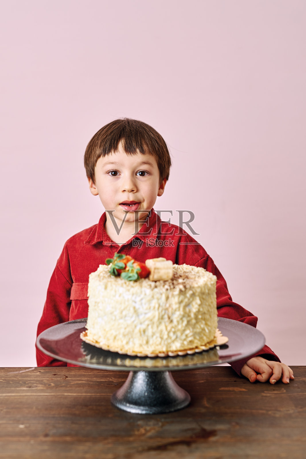 可爱的孩子在粉红色的背景上吃蛋糕。照片摄影图片