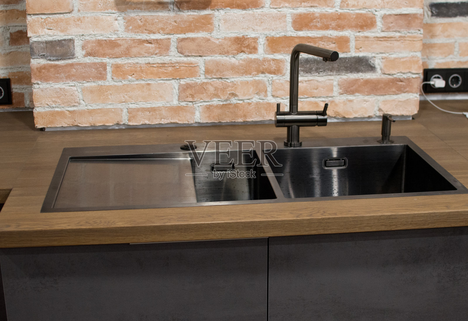 现代厨房与黑色水槽，厨房水龙头的水和面对砖墙的背景照片摄影图片