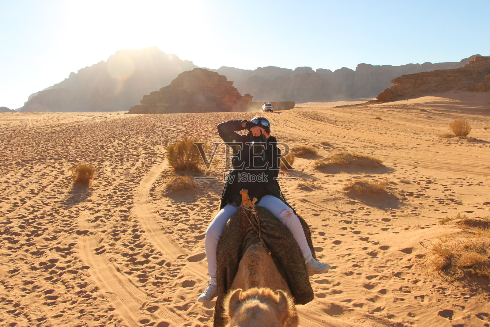 一名女子骑着骆驼，试图在沙漠中拍照照片摄影图片