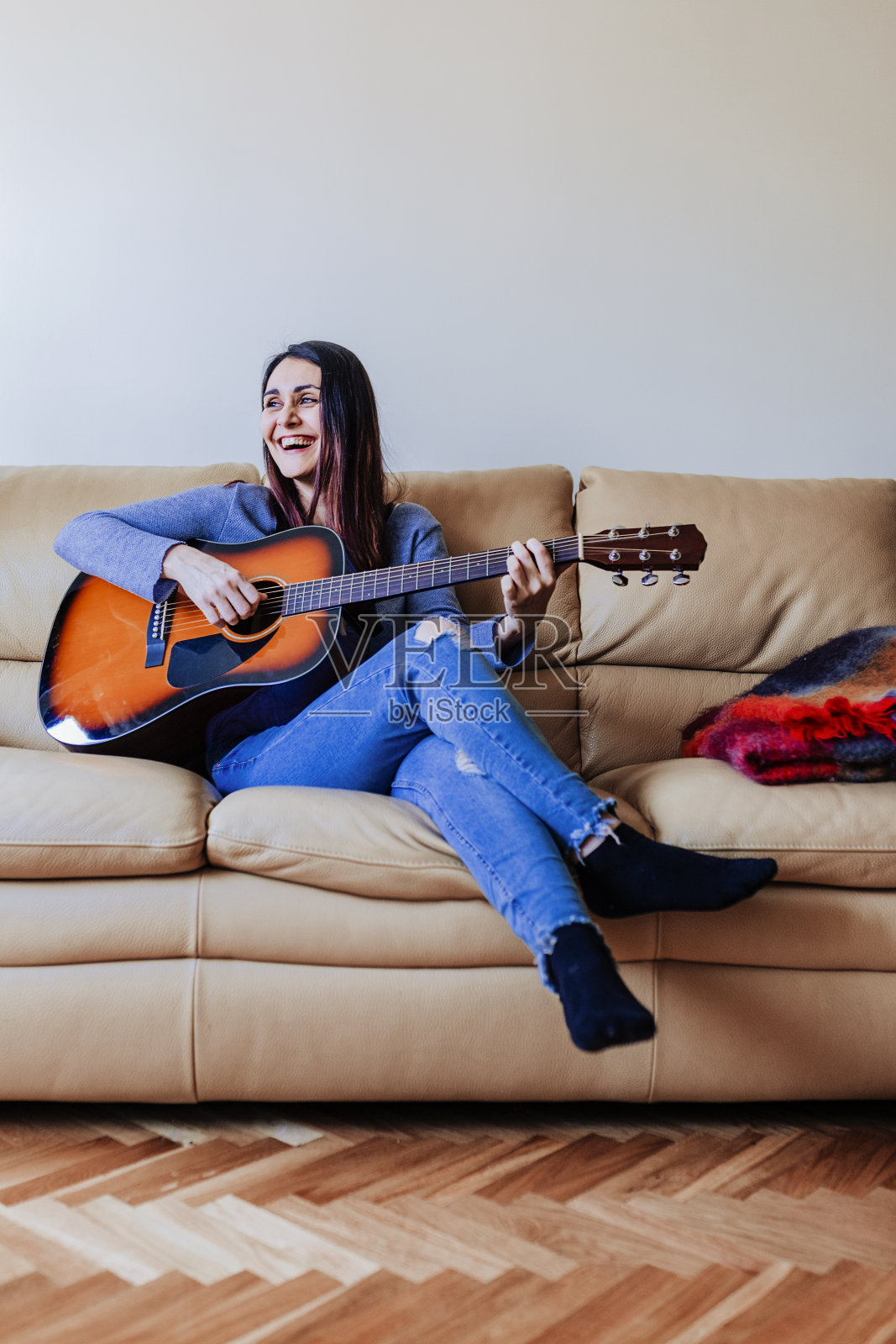 年轻漂亮的女人站在沙发上弹吉他。音乐的概念照片摄影图片