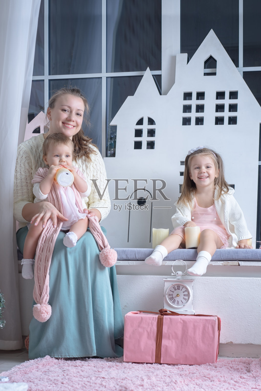 妈妈带着两个女儿靠近窗户，把玩具和礼品盒放在地板上照片摄影图片