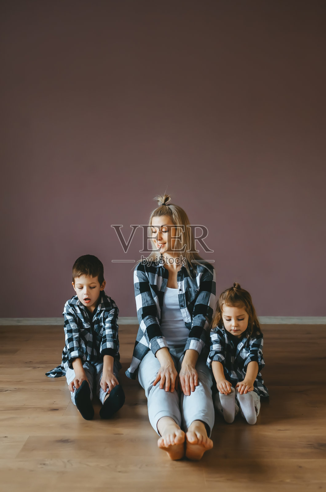 两个可爱的孩子和她美丽的妈妈穿着相同的衣服坐在木地板上。照片摄影图片