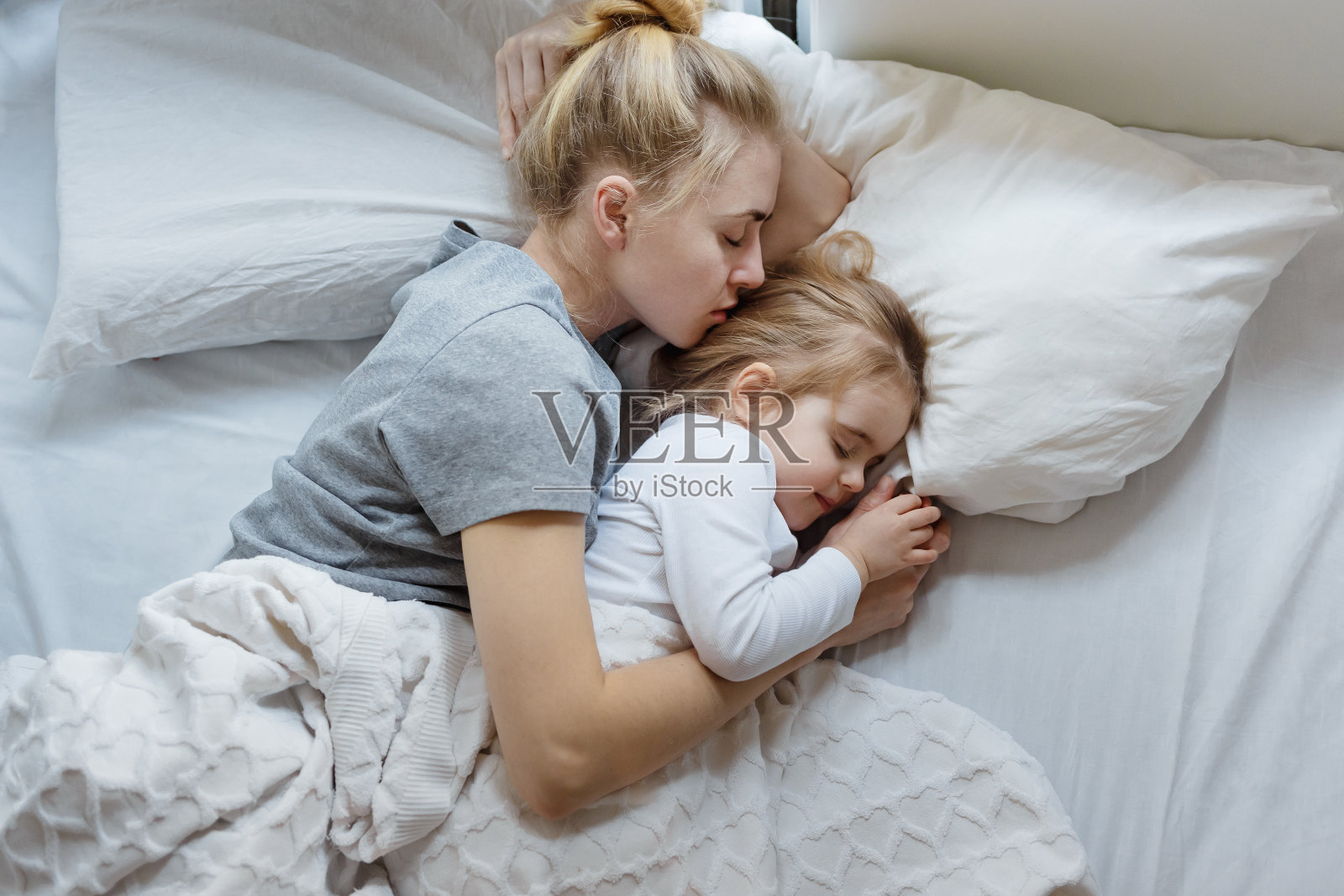 年轻的妈妈和小女儿睡在床上，俯视着copy-spaсe。安全、保护、舒适、家庭、单亲家庭照片摄影图片