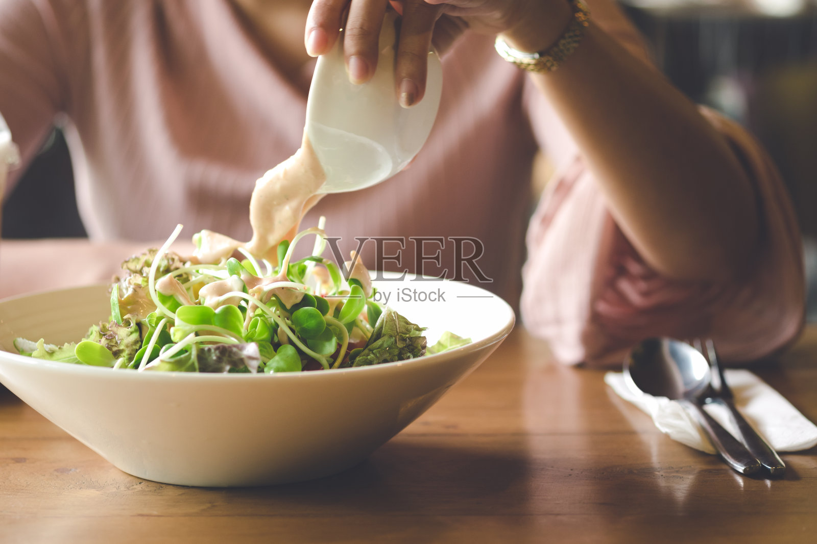 亚洲妇女的手是倒调料和吃蔬菜沙拉午餐在咖啡馆或餐厅。照片摄影图片