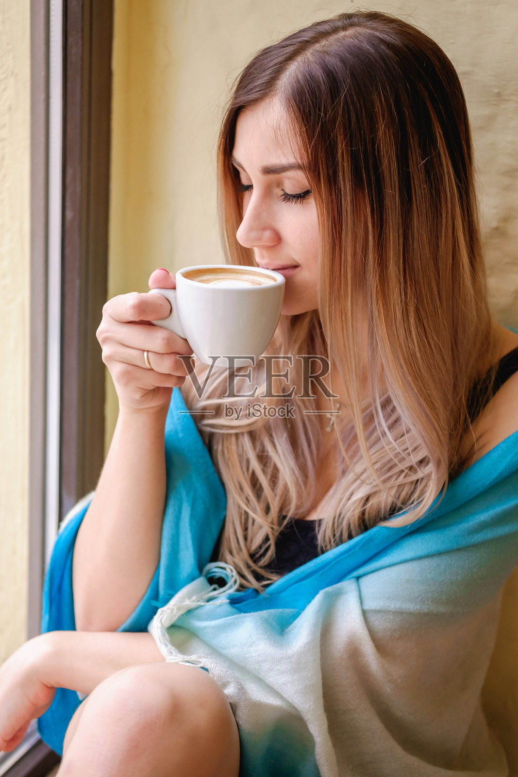 孤独的金发女孩坐在窗台上用白色的杯子端着咖啡，怀着一颗浪漫的心情照片摄影图片