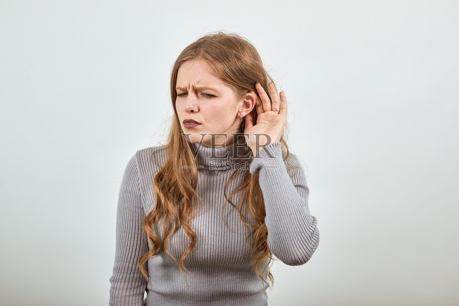 一个穿着灰色毛衣的小女孩听力不太好，她把手放在耳朵旁边。照片摄影图片