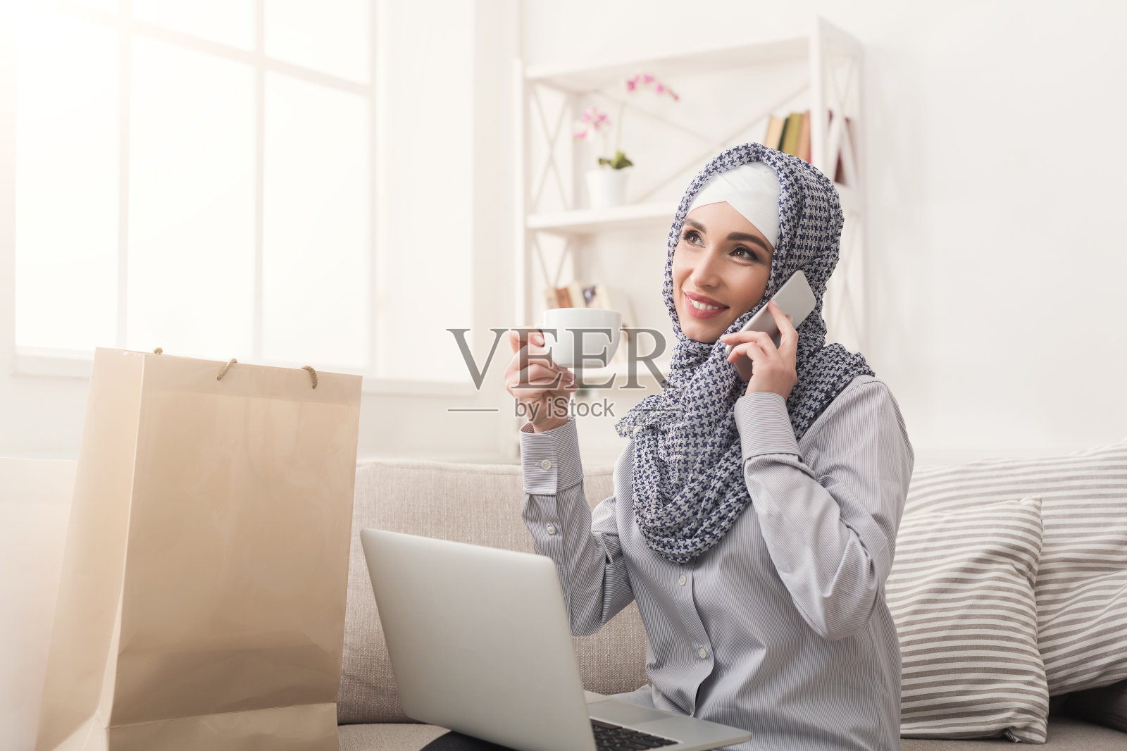 微笑的阿拉伯女人用手机聊天，在家里网购照片摄影图片