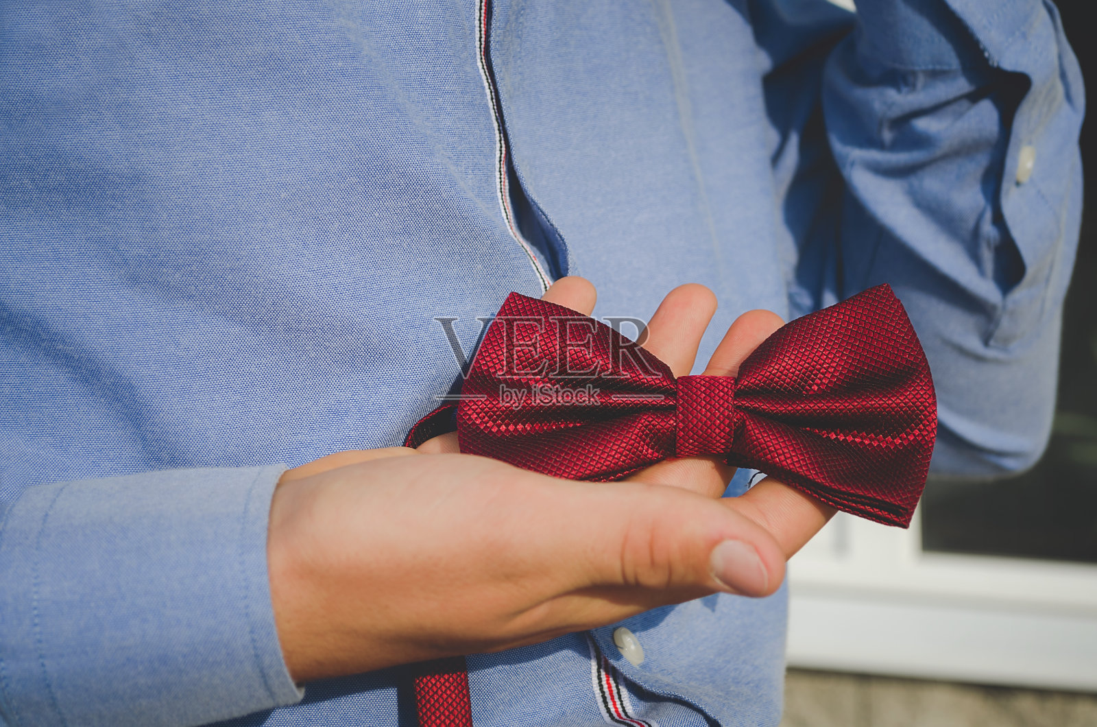 一个小男孩手里拿着一条蝴蝶形状的红领带。照片摄影图片