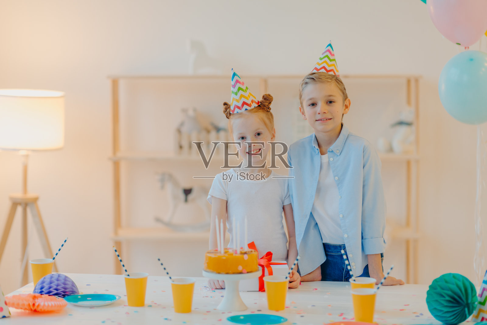 快乐的男孩和他的小姜黄色妹妹穿着节日的衣服，派对帽，一起庆祝生日，周围是蛋糕，礼物和杯酒，在特殊场合有好心情照片摄影图片