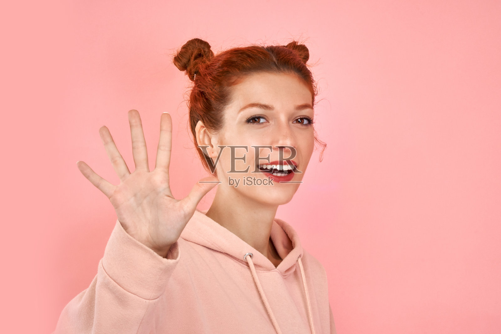 工作室的肖像白种人年轻姜妇女在时尚的服装显示问候手势或给击掌，看着相机与快乐和兴奋的表情孤立的粉色墙。肢体语言照片摄影图片