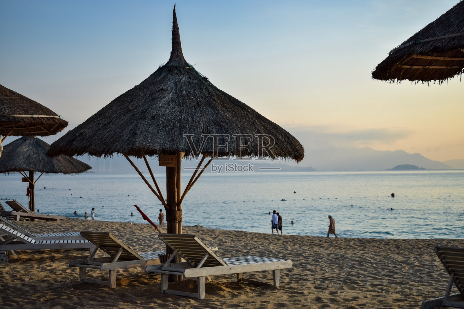拂晓时分沙滩上的草伞和海上的木制躺椅照片摄影图片