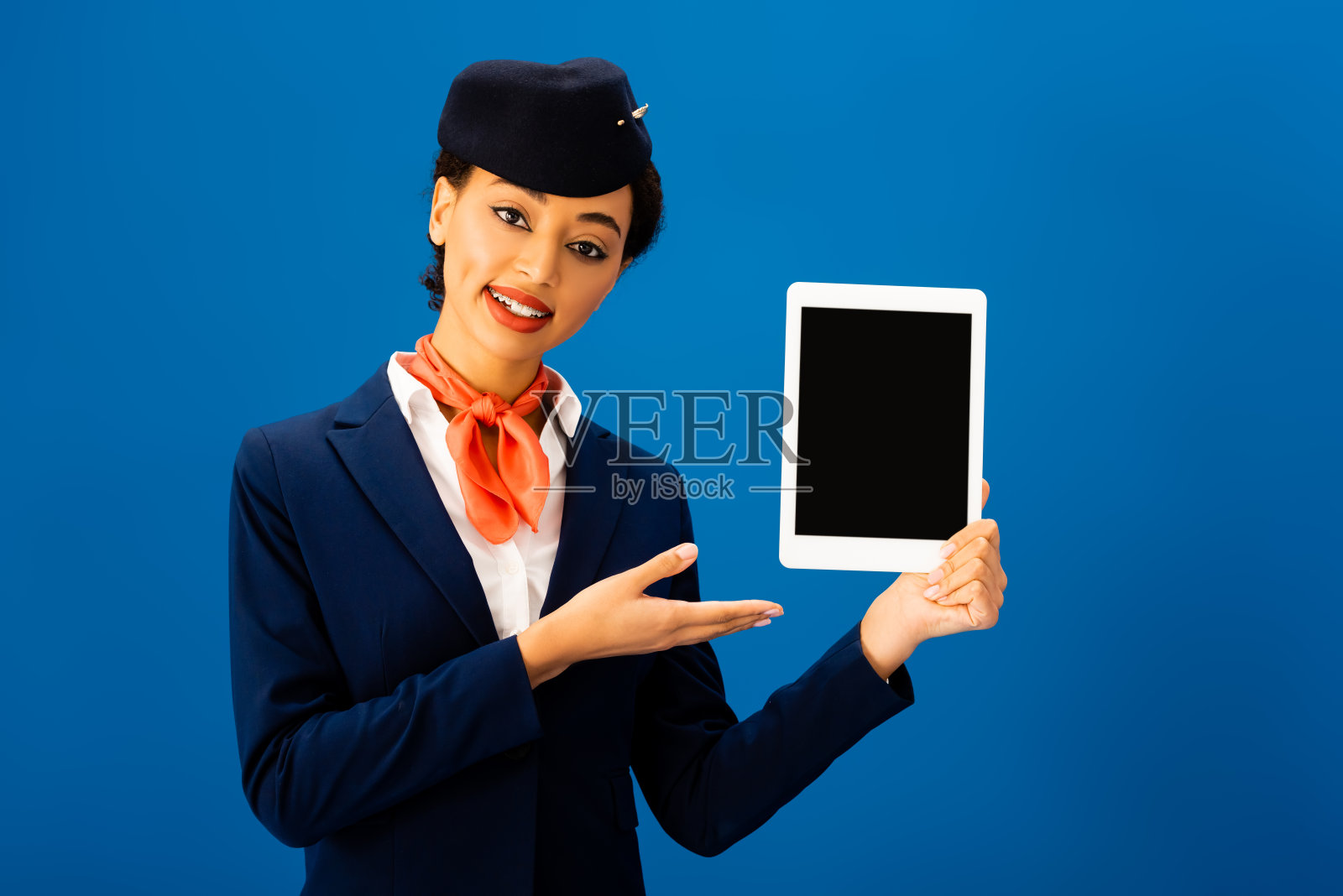微笑的非裔美国空乘用手指着孤立在蓝色的数字平板电脑照片摄影图片
