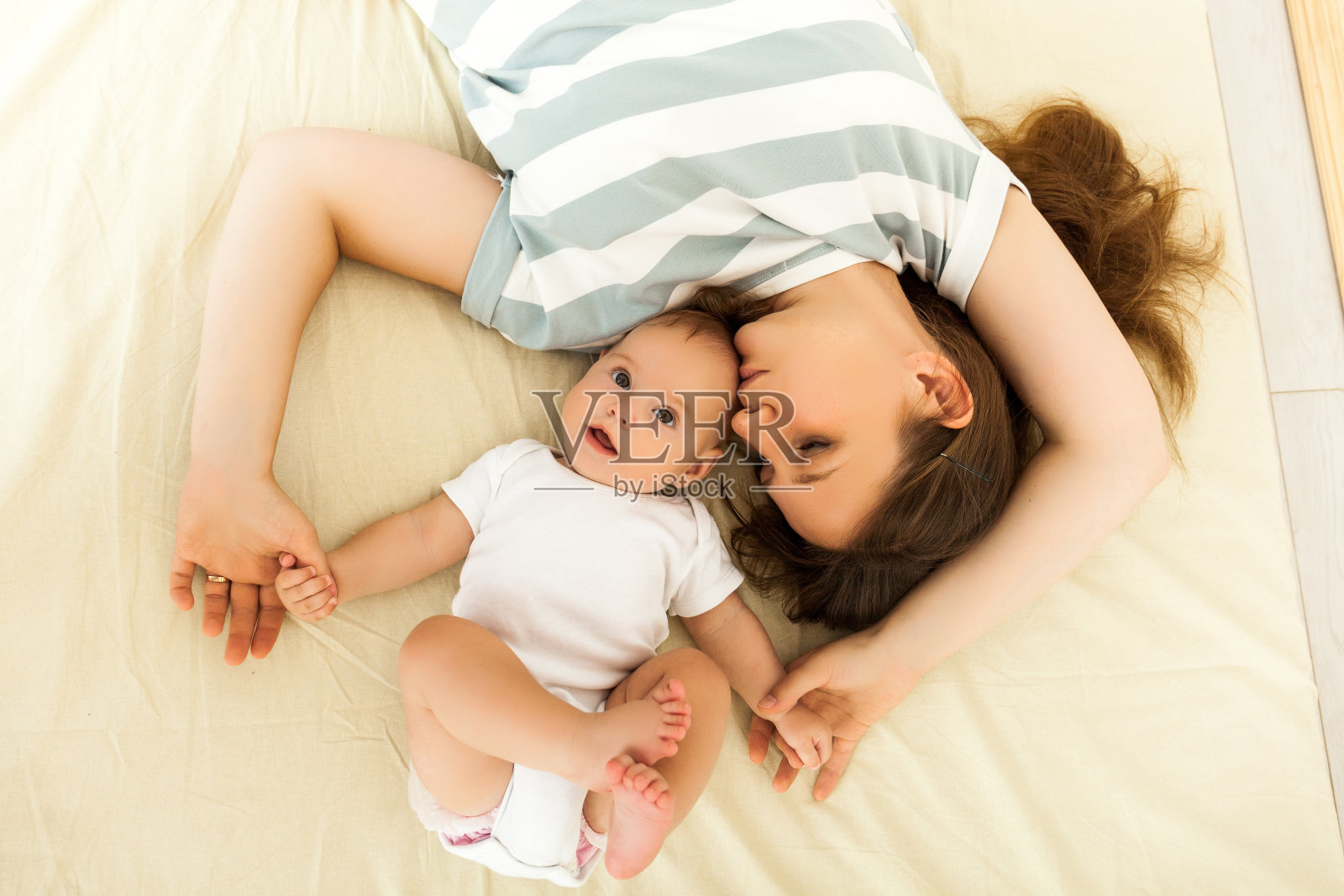 快乐的妈妈亲吻躺在床上的婴儿照片摄影图片