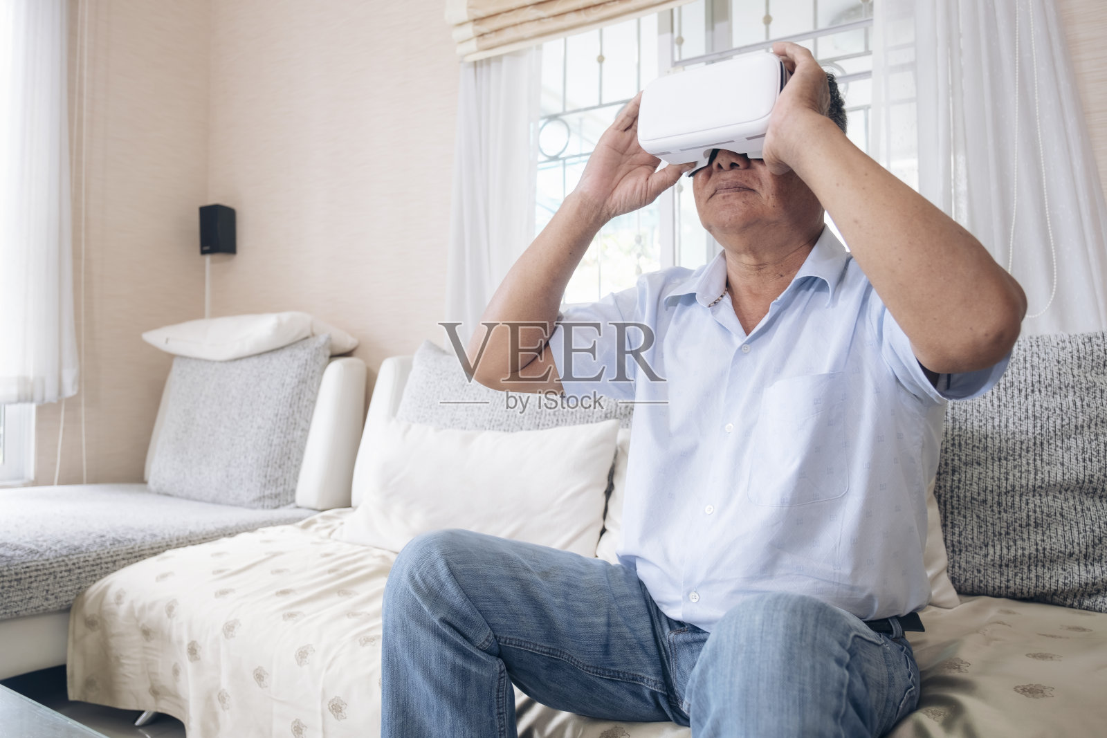高级男子在沙发沙发上使用VR头盔在家。照片摄影图片