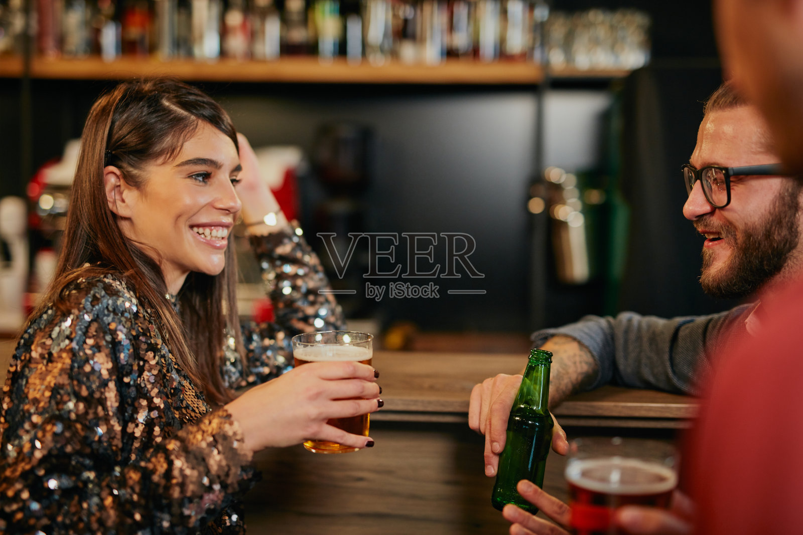 一对白人夫妇靠在吧台上，喝着啤酒聊天。夜生活。酒吧室内。照片摄影图片