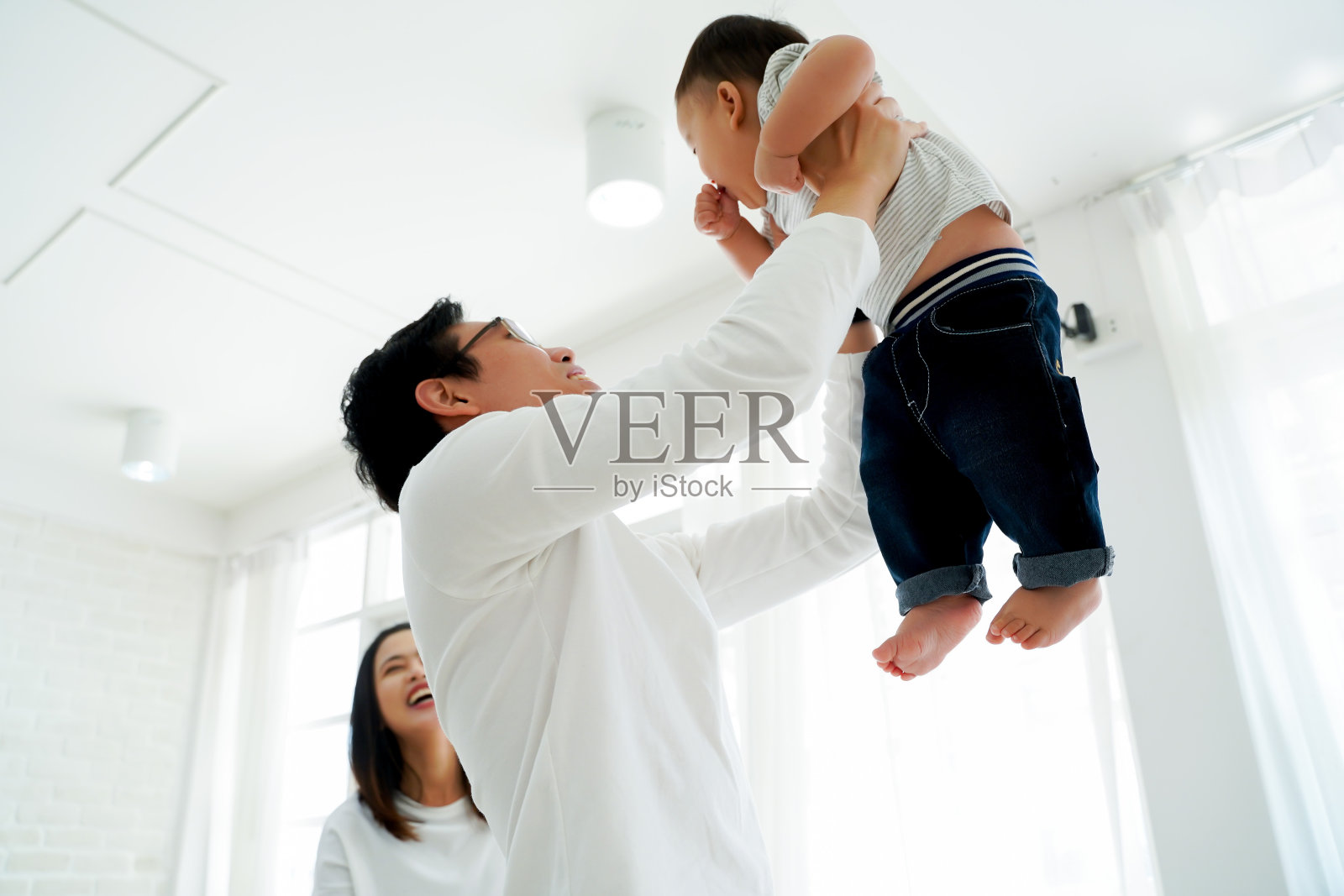 亚洲的父亲和母亲就像一对夫妻，把自己的儿子高高举起，在笑声和幸福中飞向空中。他激动得情绪高涨。亚洲的亲子观念照片摄影图片