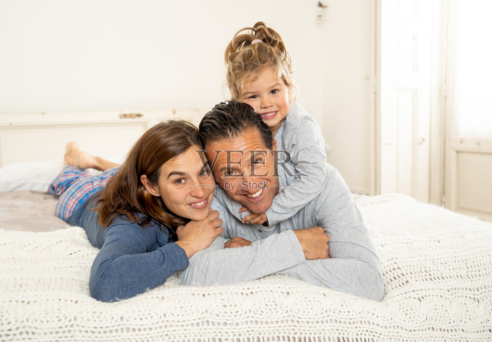 生活方式的肖像美丽幸福的家庭放松和花时间一起在床上在家。妈妈，爸爸和可爱的蹒跚学步的女儿在早上有有趣的亲吻拥抱和亲密。照片摄影图片