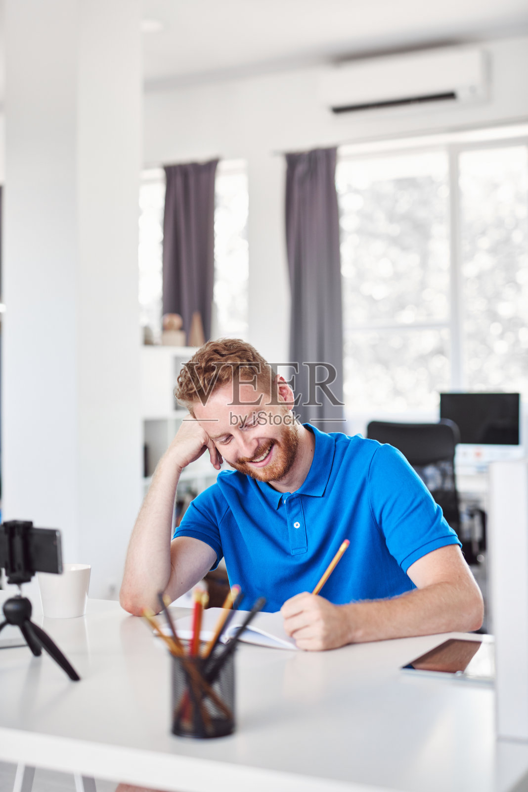 开朗的高加索姜黄色员工坐在他的办公室里，在笔记本上写他的任务。照片摄影图片