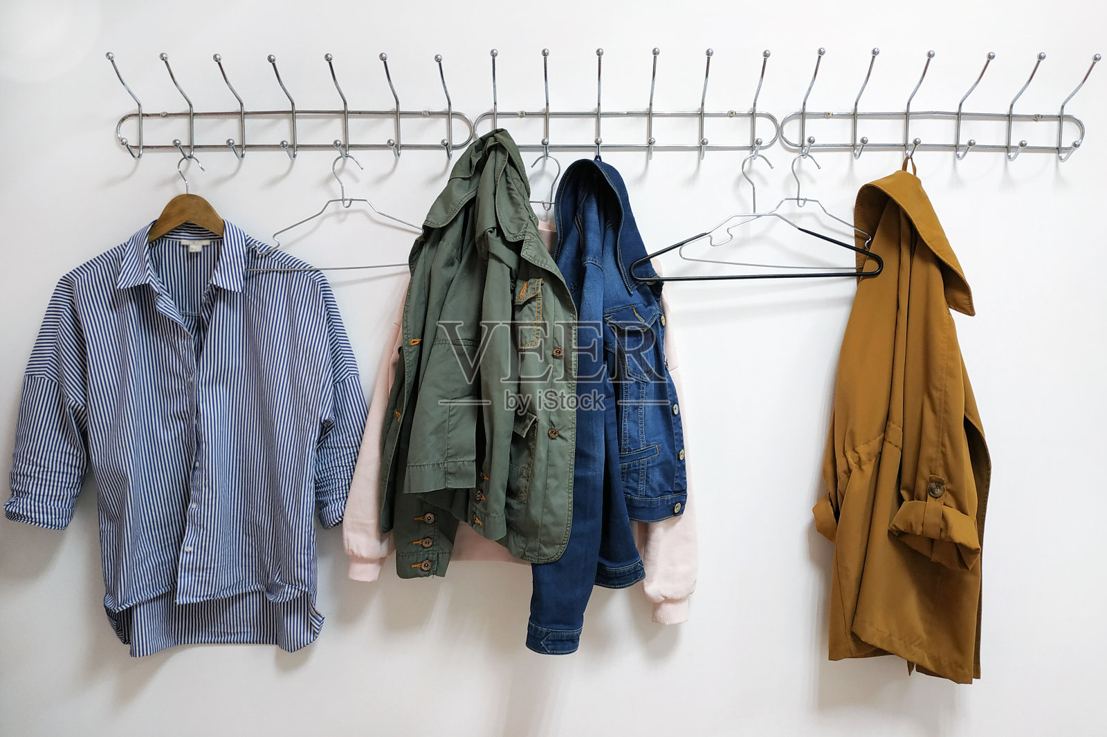 一件衬衫、夹克和一个衣架挂在金属的墙上衣架上。照片摄影图片