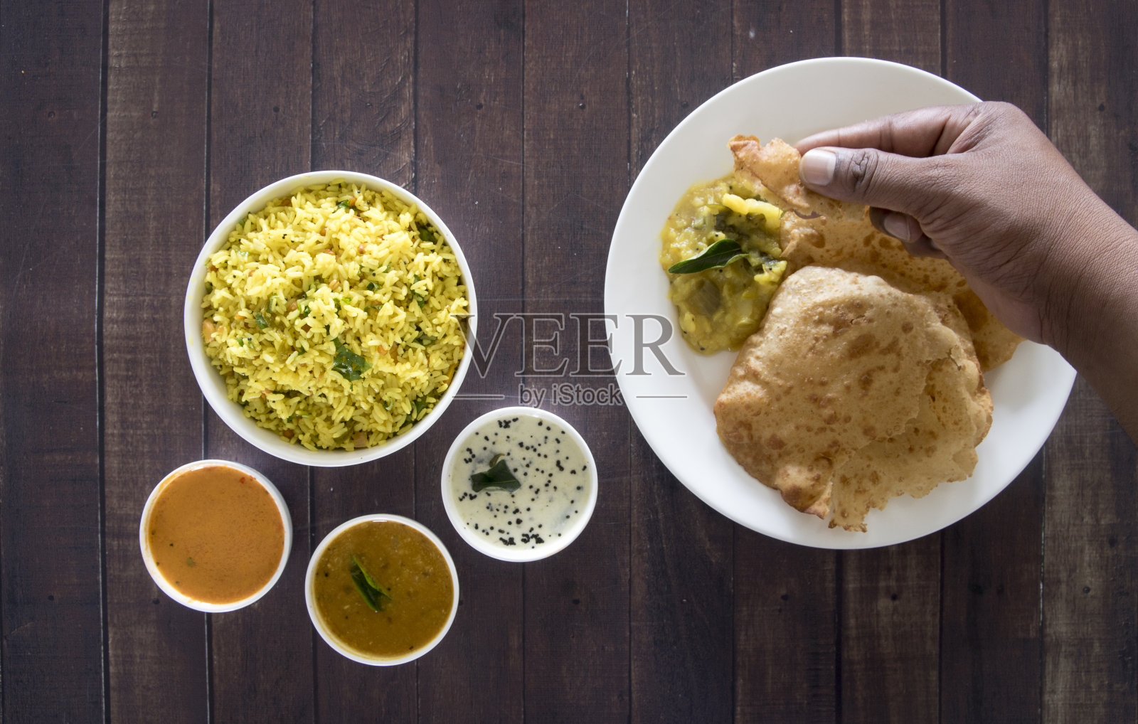 一只印度手正在采摘印度食物Poori。木桌上的印度食物俯视图照片摄影图片