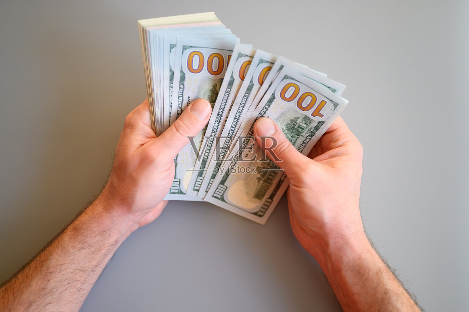 男人的手握着并数着灰色背景上的100美元钞票照片摄影图片